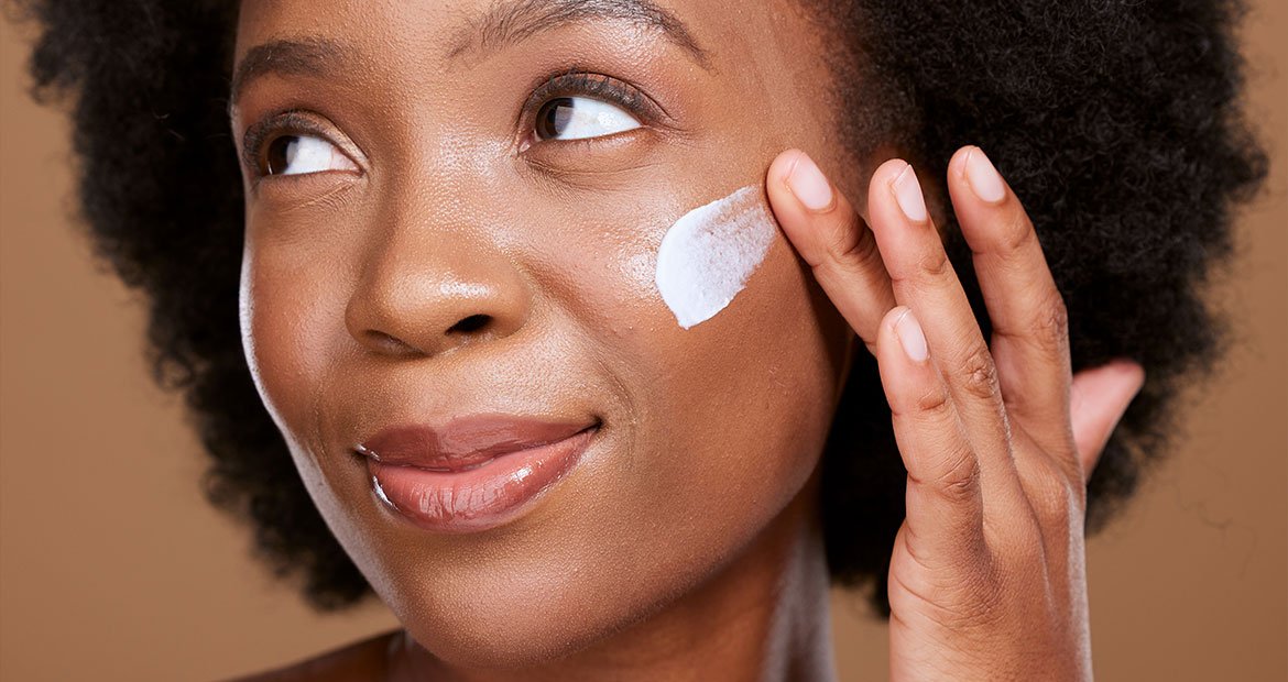 mulher negra passando levemente sorridente passando creme no rosto